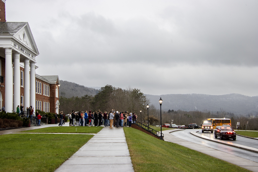 emergency vehicles lead the school bus in front of crowd at school
