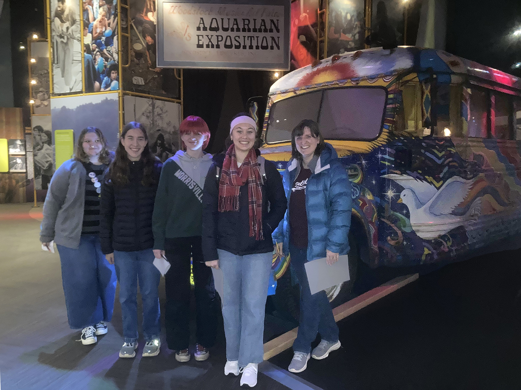 4 students and a teacher pose in the Museum at Bethel Woods