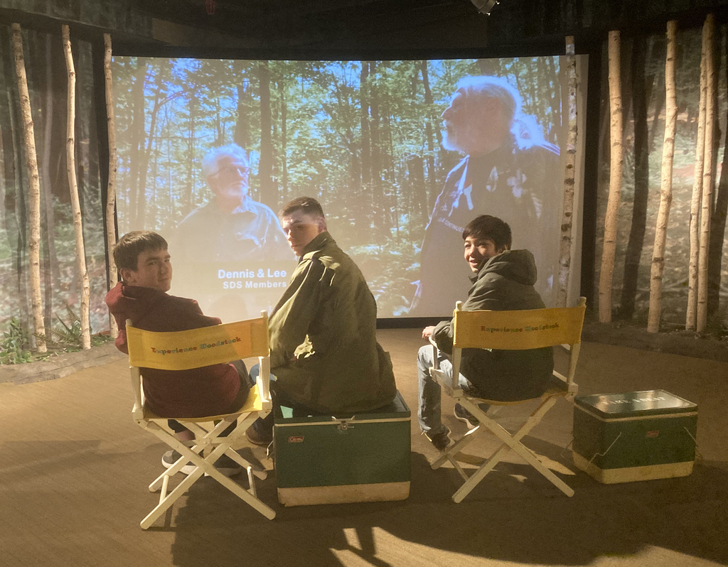 3 student in directors chairs in one of the museum's display areas