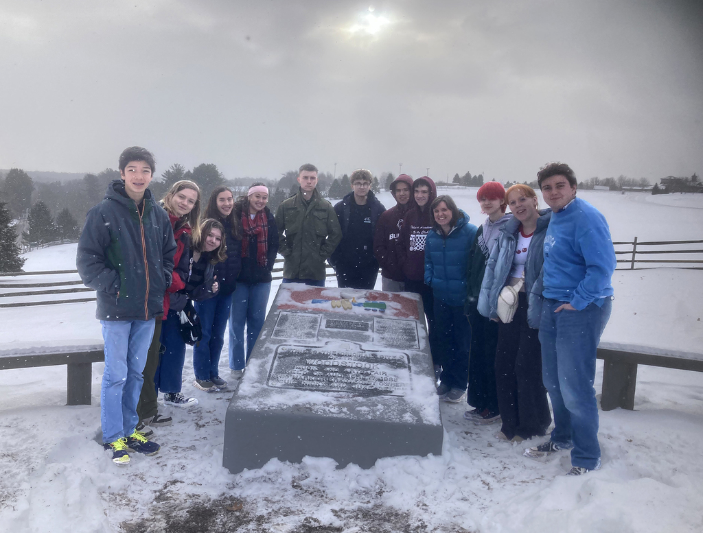 12 students and a teacher pose around the Woodstock Music Festival monument