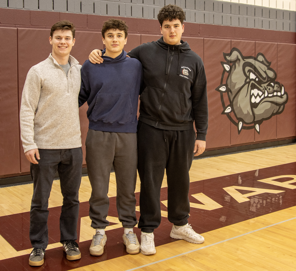 Adam Cook, Lucas Nealis and Steven Hillis pose in front of Bulldog logo
