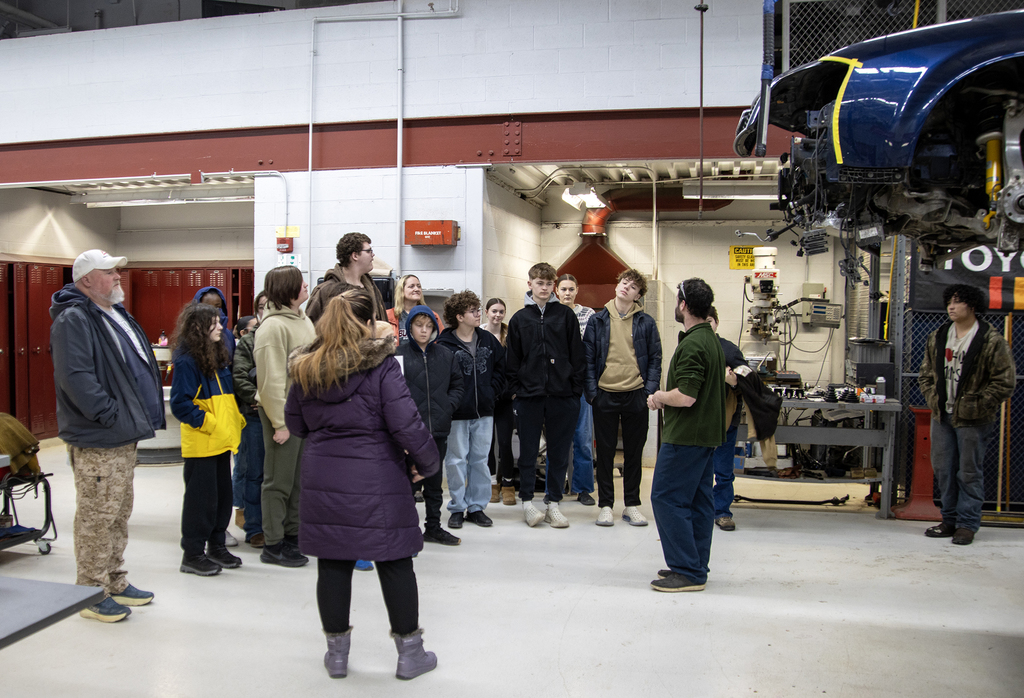group of students andtwo teachers with auto tech instructor in auto lab