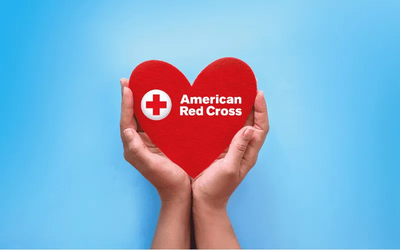 cupped hands holding a red heart with "American Red Cross" logo on it