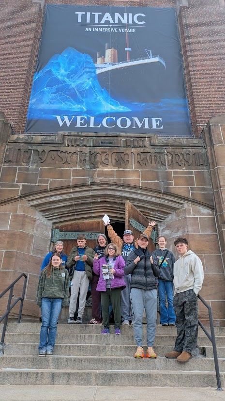 students pose outside the armory under sign that says Titanic: An Immersive Voyage
