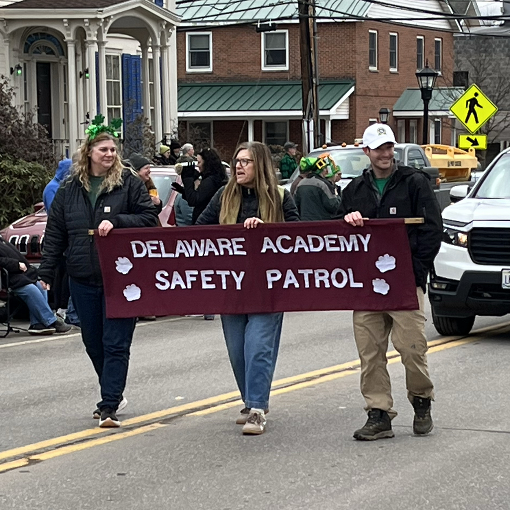 3 adults carrying banner that says Delaware Academy Safety Patrol