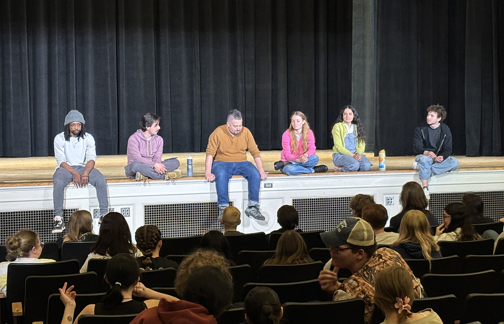 the theater group sits on the edge of the stage and answers questions