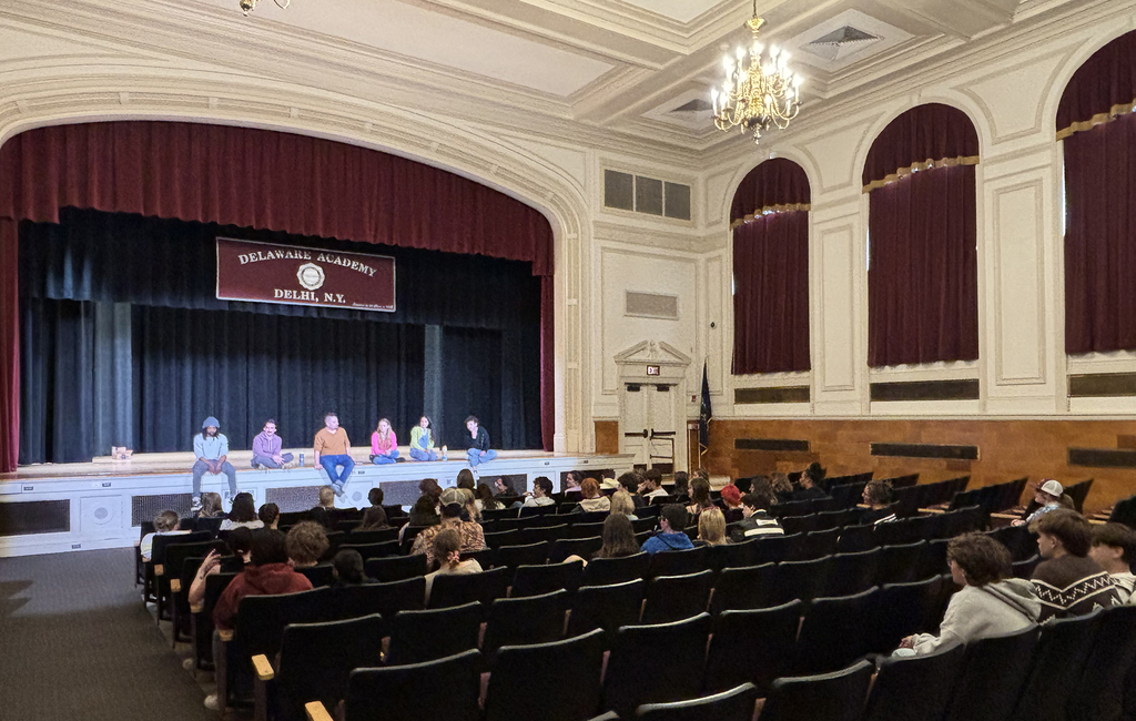 the theater group sits on the edge of the stage and answers questions