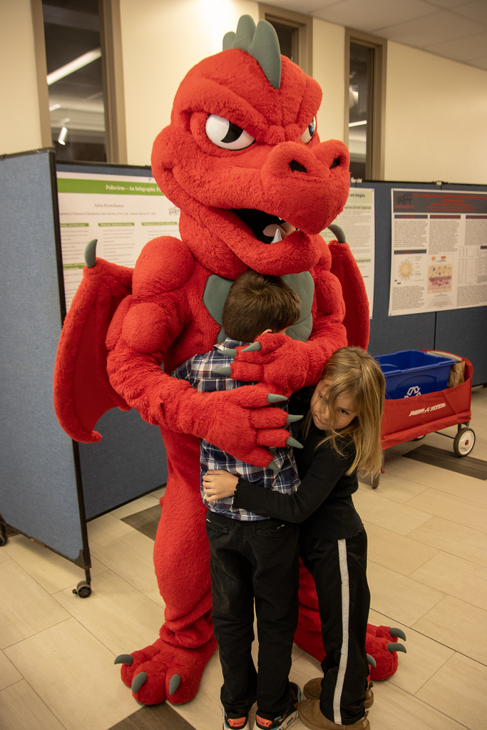 Red the Dragon mascot hugs two children