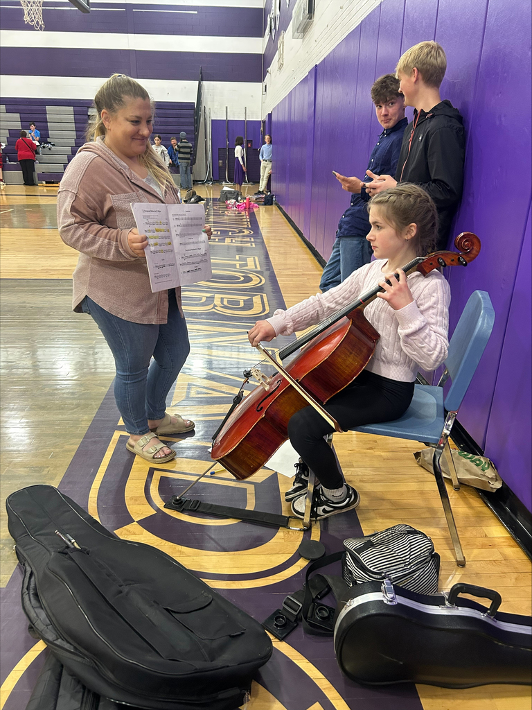 A student practices cello while her mother holds her music