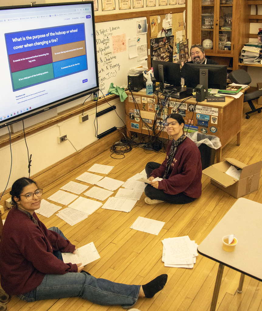2 students in Mr. All's room sort papers on the floor