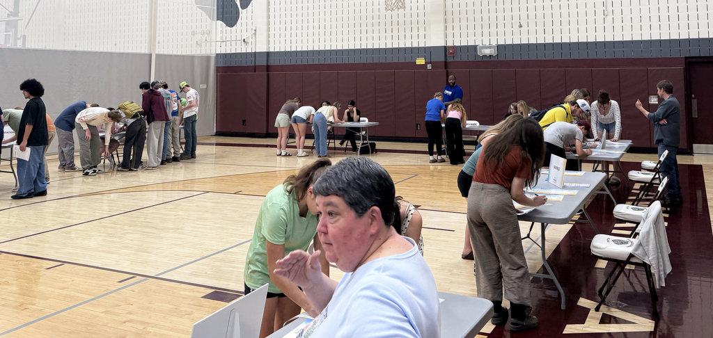 students gathered around tables; Mrs. Sherman talking in foreground