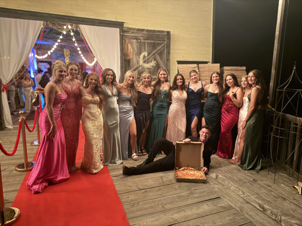 13 girls in prom gowns and a boy in a suit with a pizza box