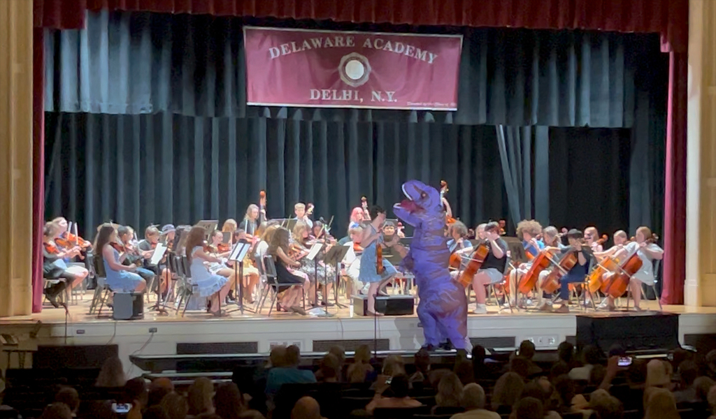 student in dino costume conducting orchestra