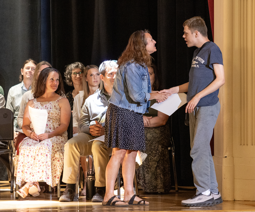 Mrs. Nealis congratulating Evan Kruppo; other teachers look on