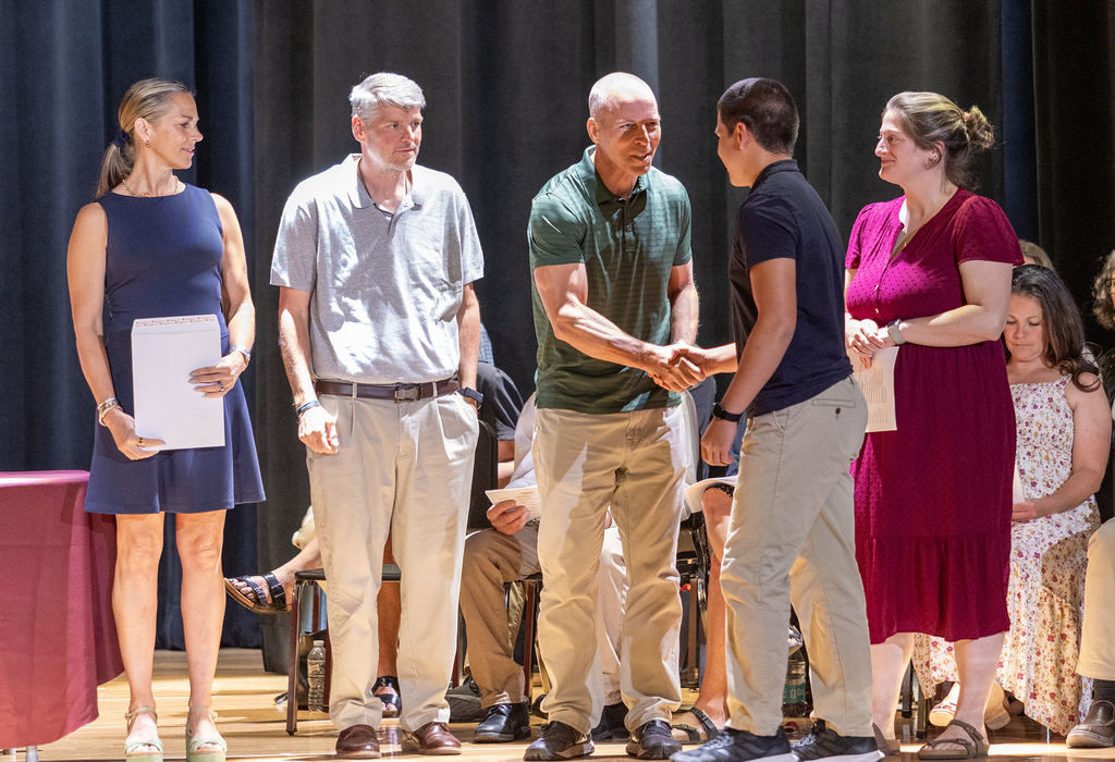 student shaking hands with one of 4 teachers on stage