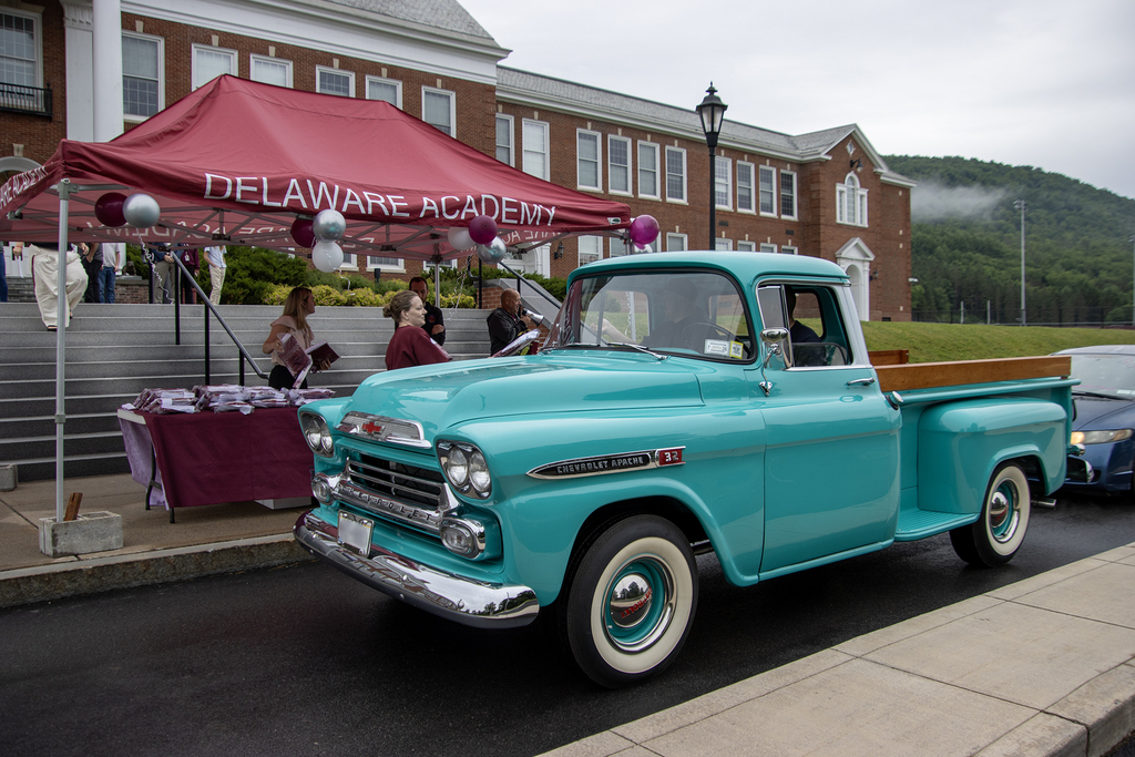 student in a vintage pickuip truck picking up his cap and gown in front of the school