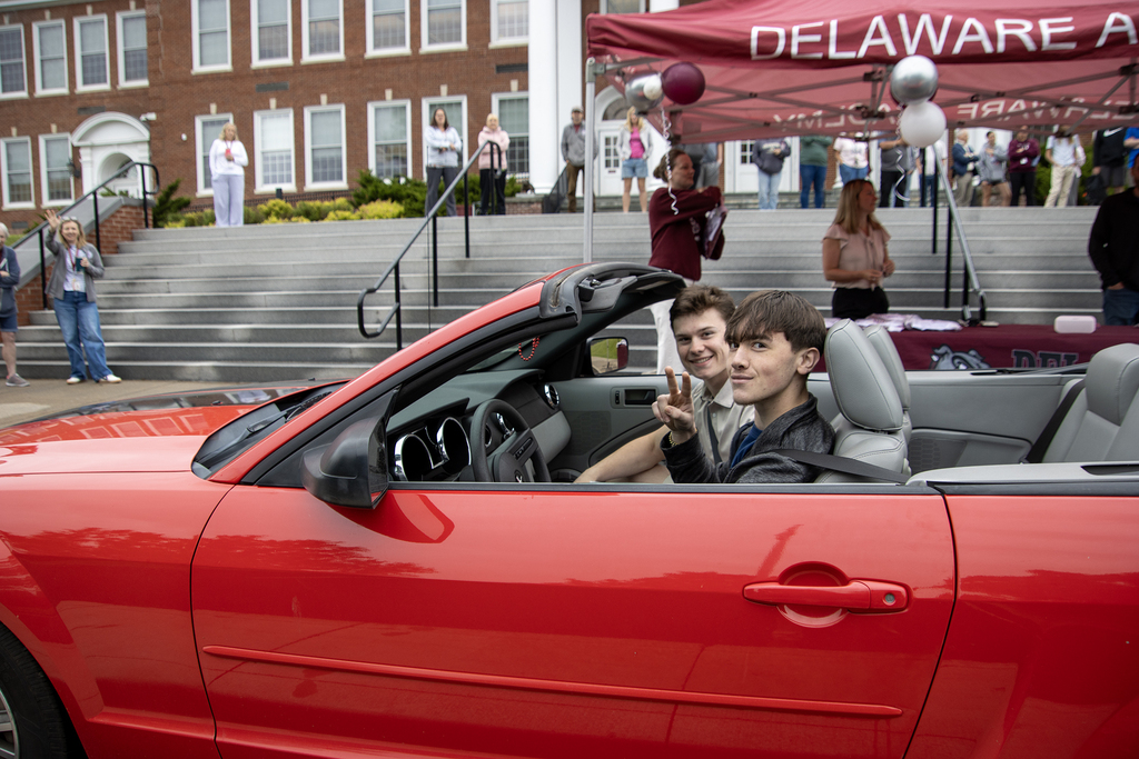 students in convertible picking up their caps and gowns in front of school