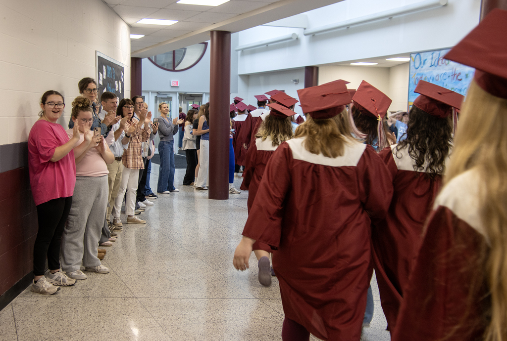 seniors in caps and gowns walk through the hallway of middle school, people applauding