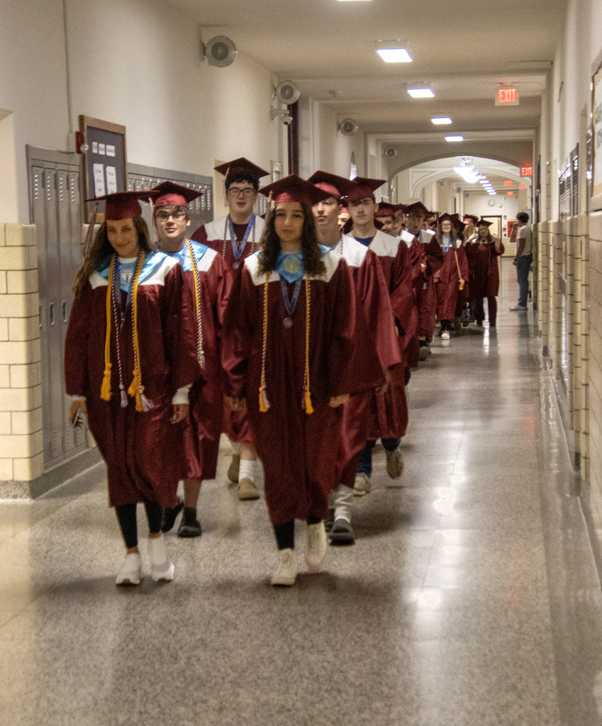 seniors in caps and gowns walk through the hallway