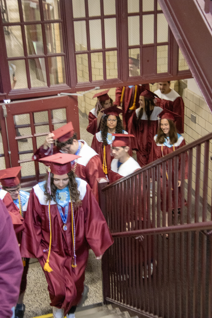 seniors in caps and gowns walk up the stairs