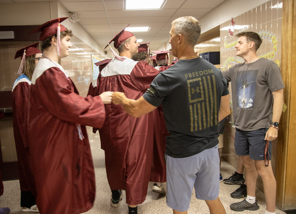 seniors in caps and gown fist bump with a teacher