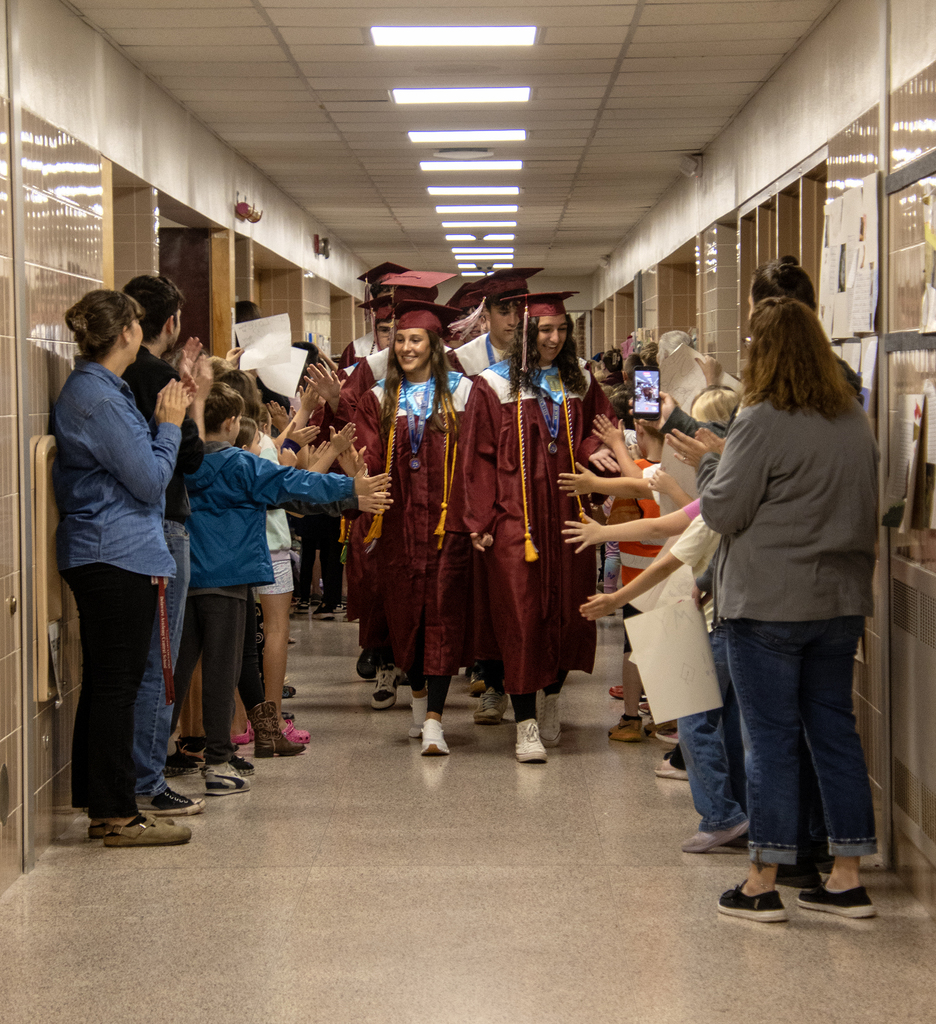 seniors in caps and gowns walk through the hallway, students offering high fives
