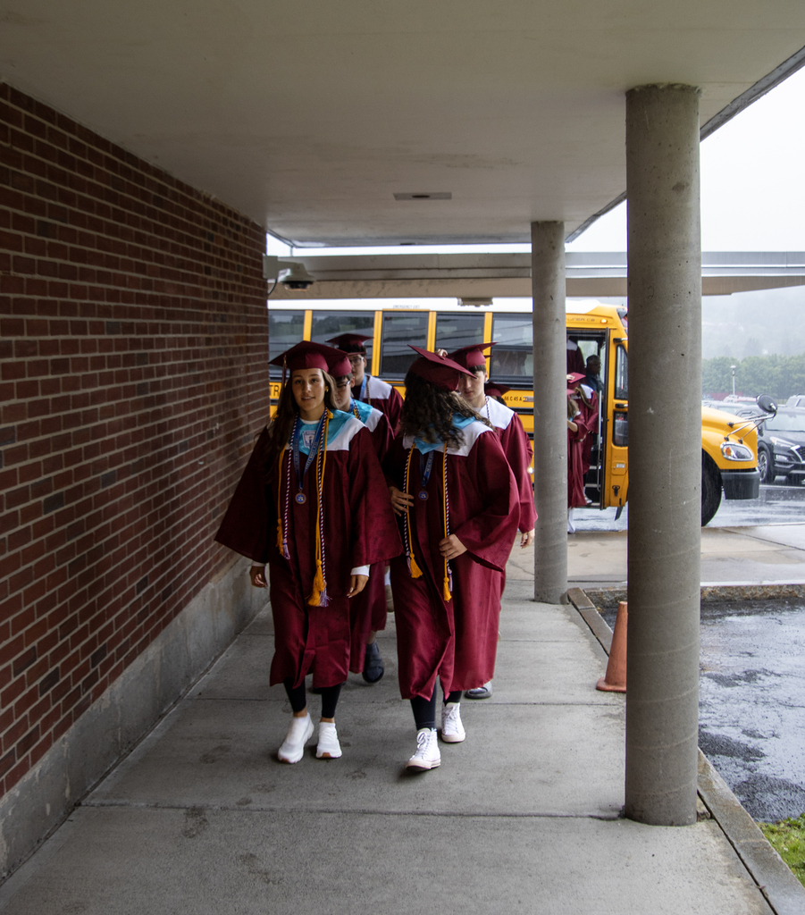 seniors in caps and gowns walk under an overhang to the elementary school