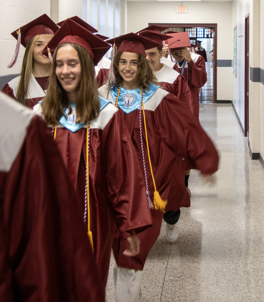 seniors in caps and gowns walk through the hallway