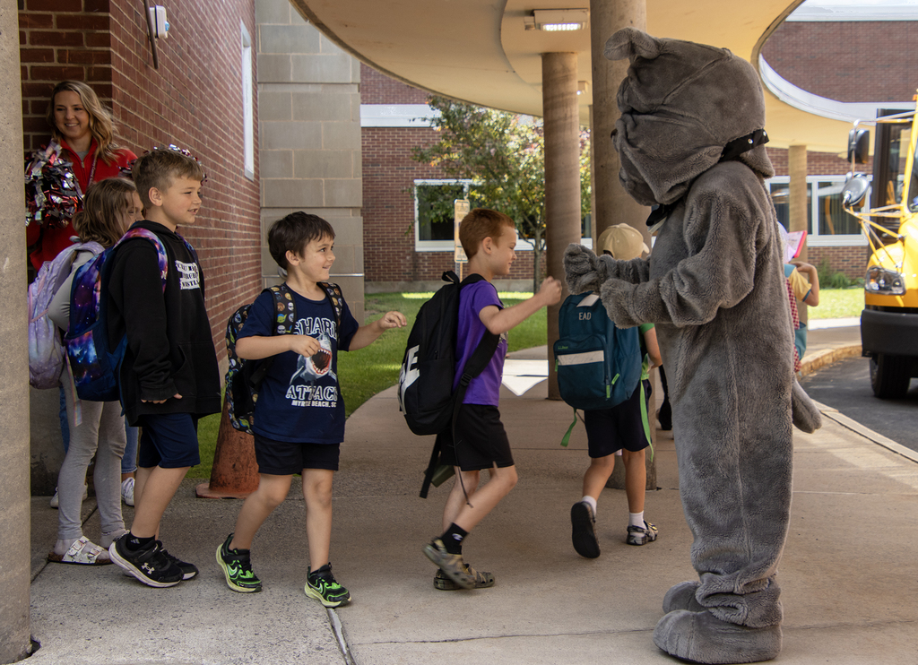students fistbump the Bulldog mascot as they leave school