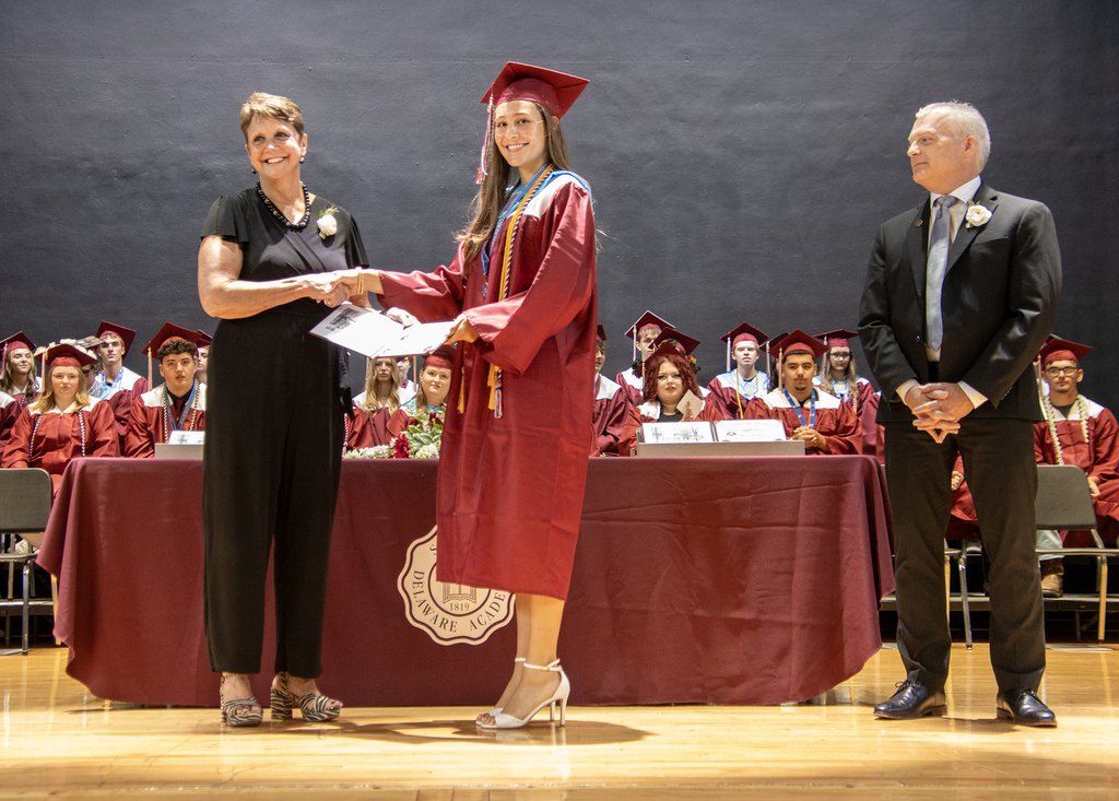 valedictorian receivng diploma from board president while the superintendent looks on