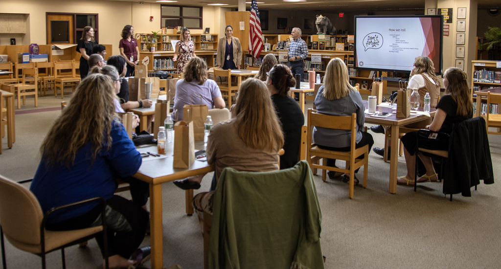 Mr. Shultz and 4 principals standing, talking to the seated new hires in the library
