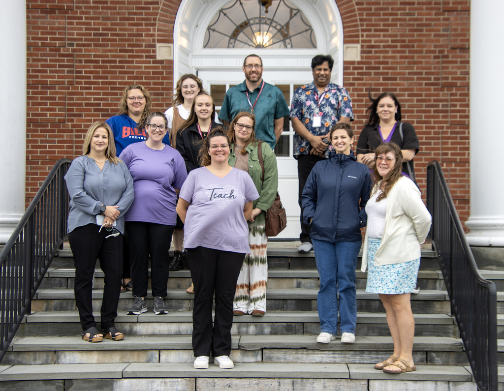 Group photo of 12 new employees on the steps of the school