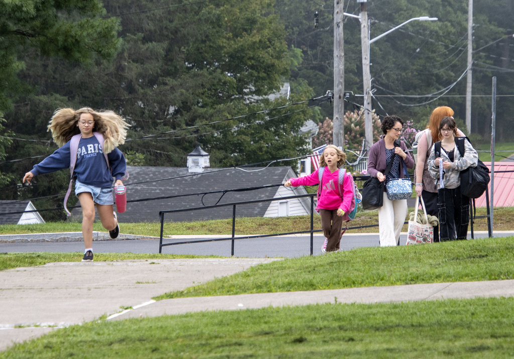 Two Gibson girls walking to school; their mother is behind them talking to high school students