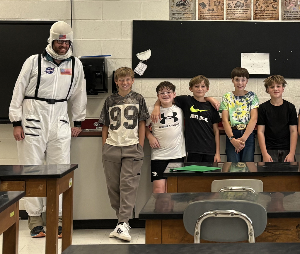 Mr. Snedeker wearing an astronaut suit and 5 boys lined up in front of classroom