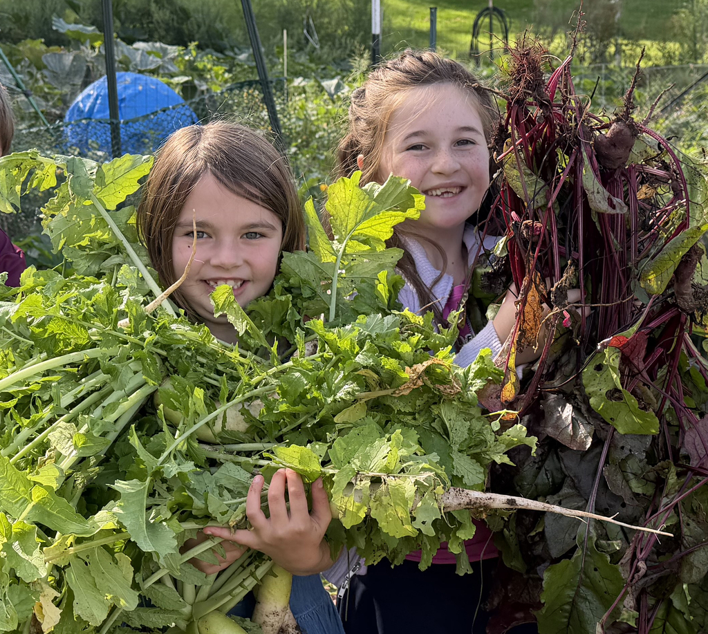 2 third grade studeents pose with armloads of leafy vegetables