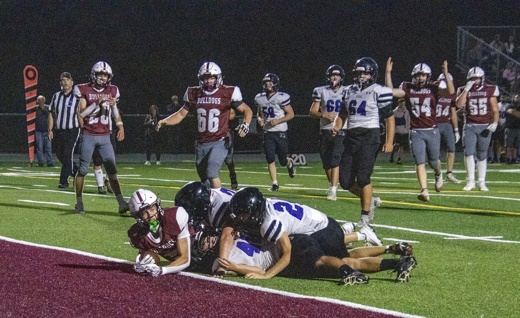 DA football player lies with ball just across the goal line sith several tacklers on top of him