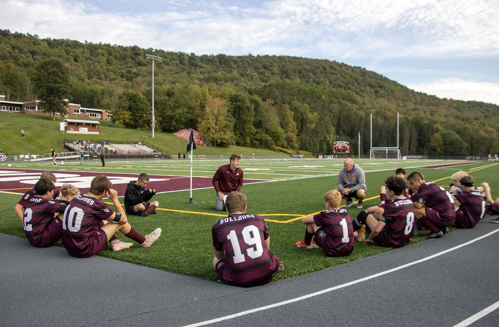 coach speaking to seated players on the corner of the soccer field