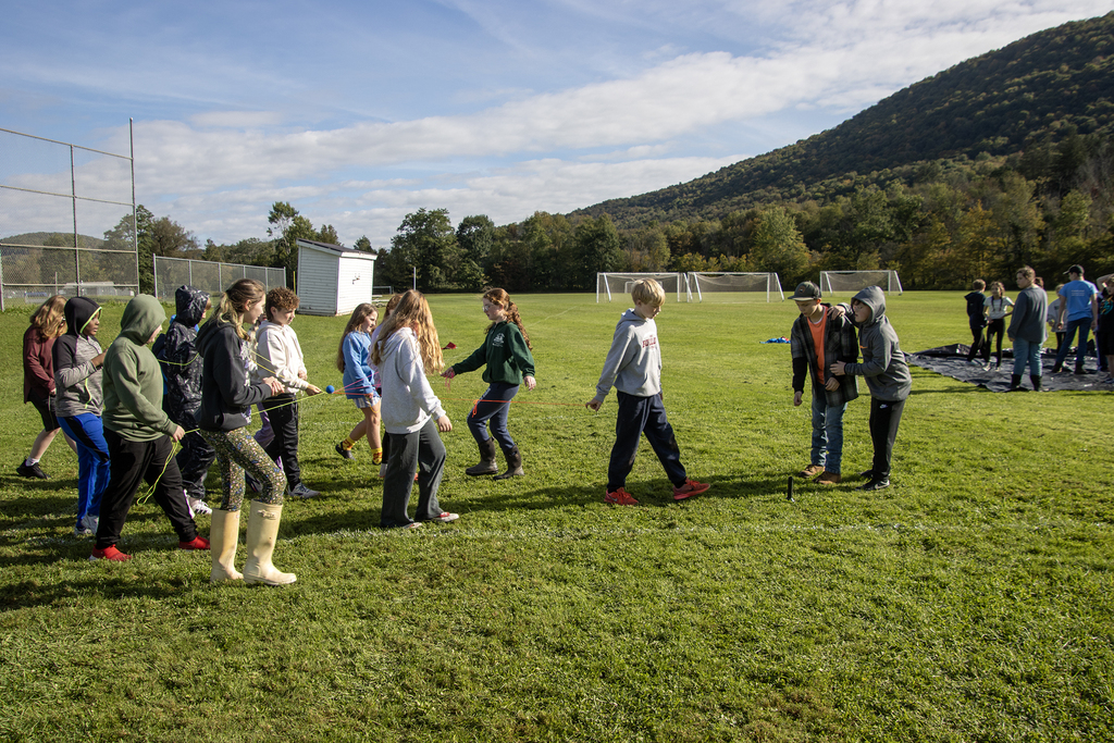 students holding strings tied together to form a web are carrying a small ball