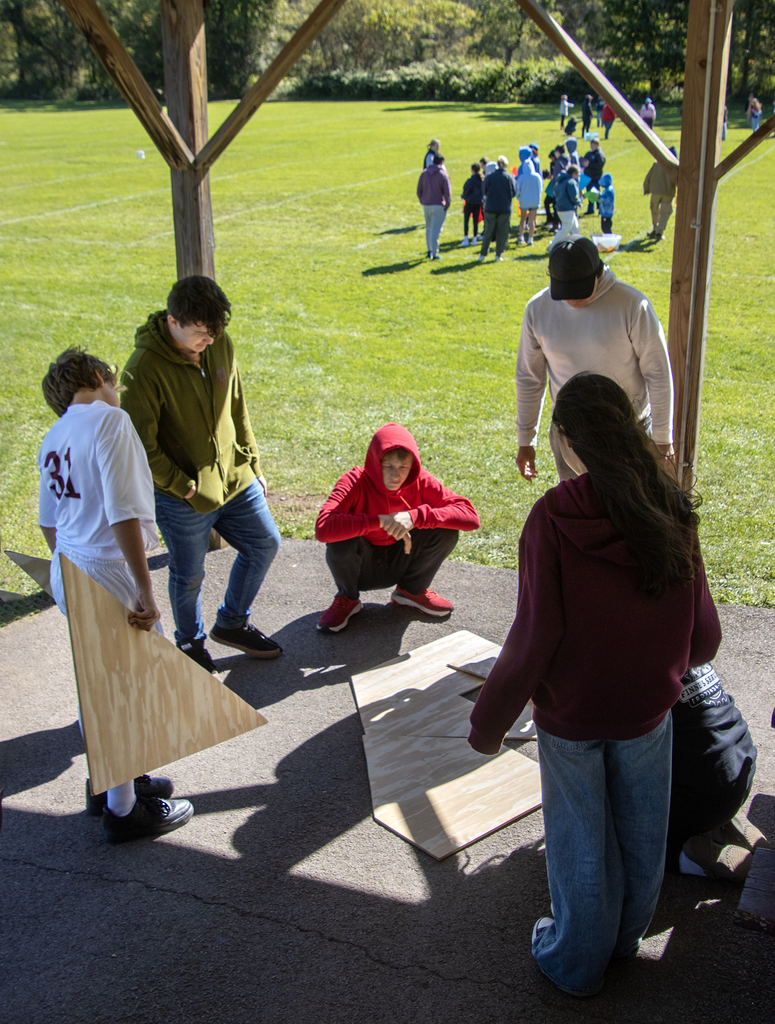 5 students work on solving a puzzle with large plywood pieces