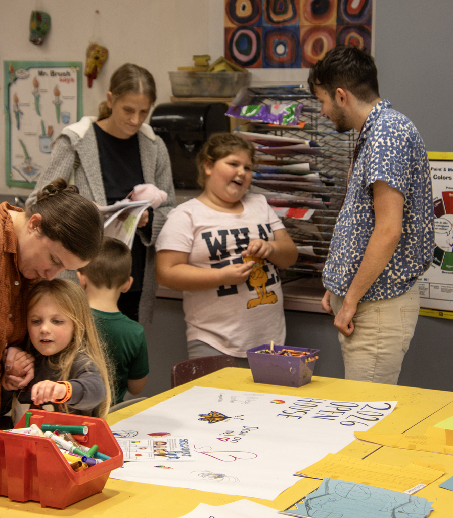 student talks to art teacher, other child holds hand with a parent and reaches for a marker, mom is standing