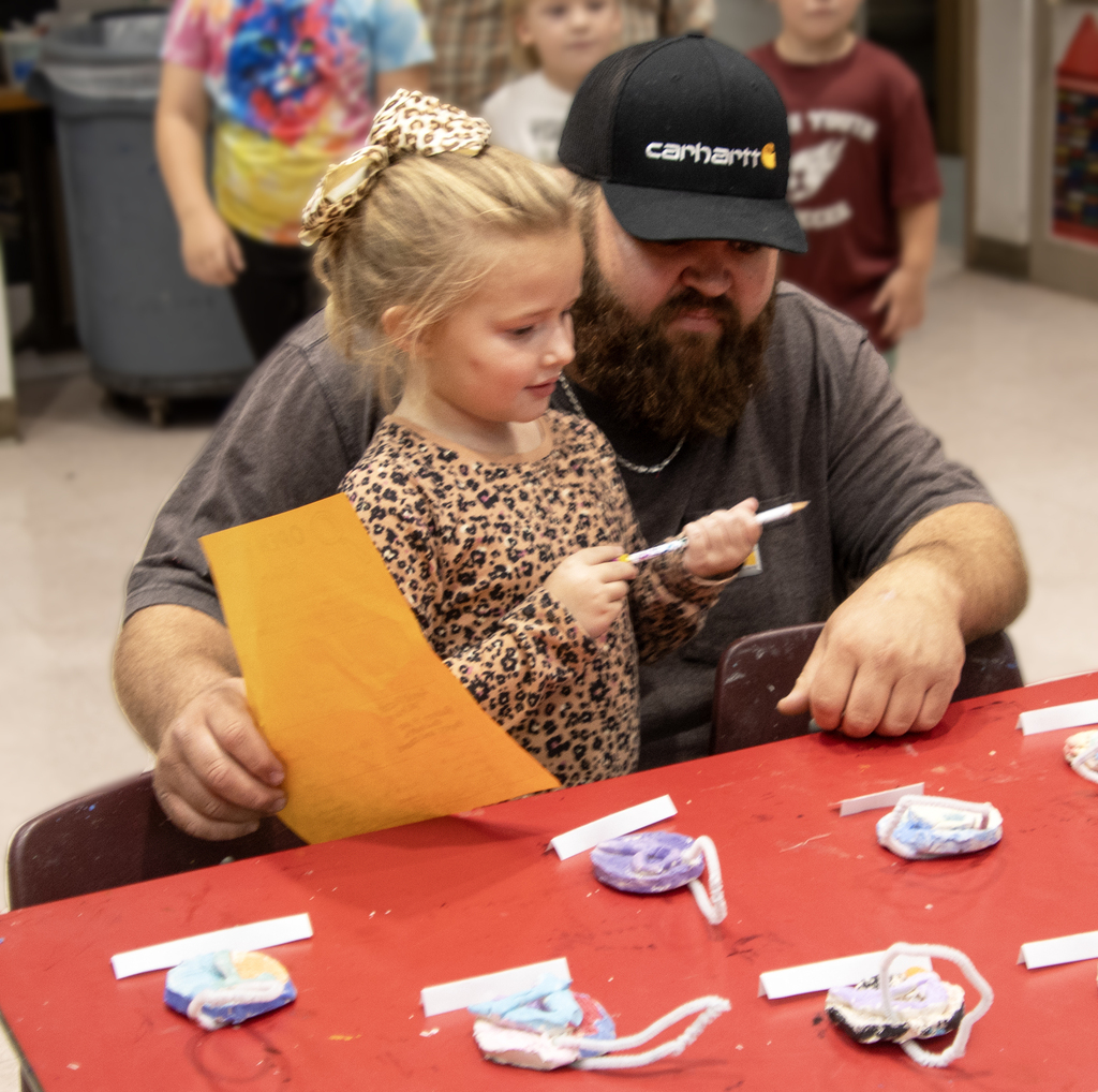 dad with arm around daughter, looking at art on table in classroom
