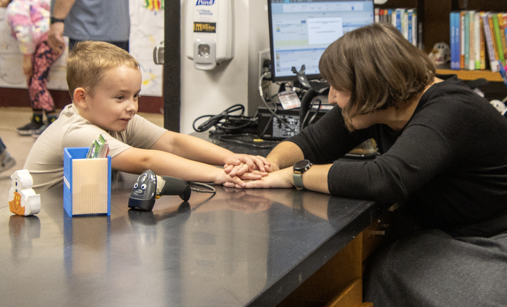 boy holds hands across counter with school librarian
