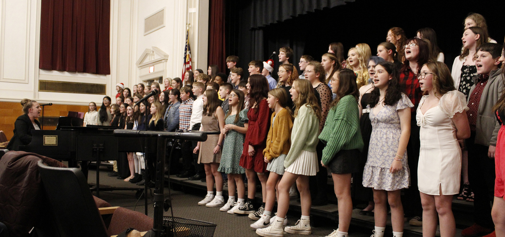 Music teacher singing and conducting and playing the piano, the chorus is singing along