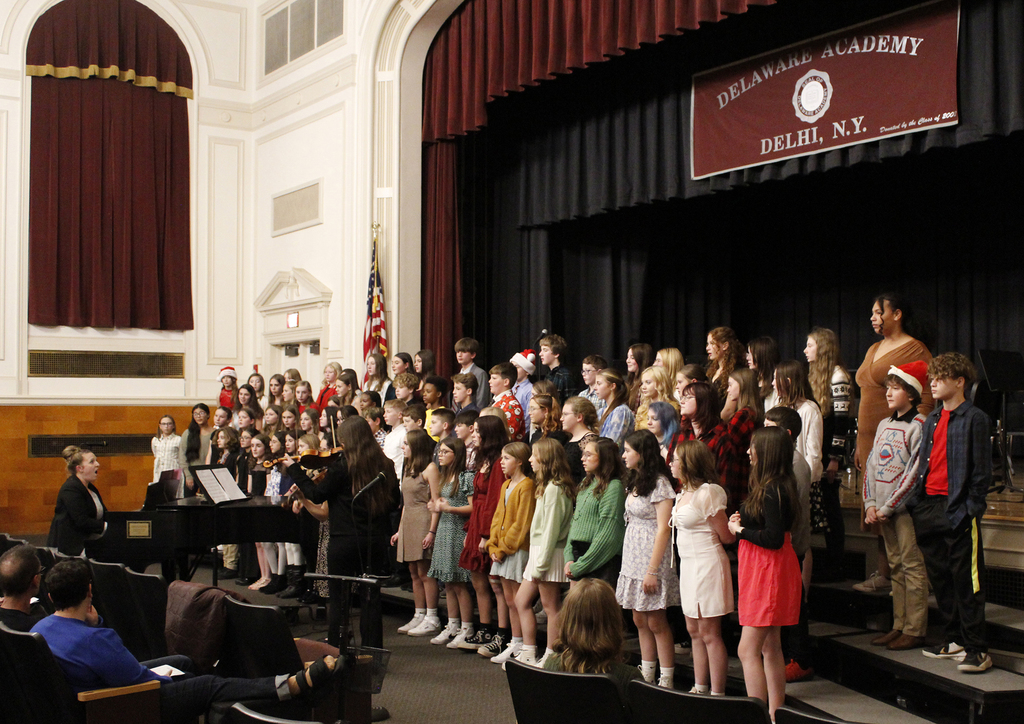 Music teacher singing and conducting and playing the piano, the chorus is singing along