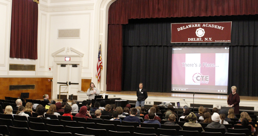 3 adults present to a group of students in an auditorium