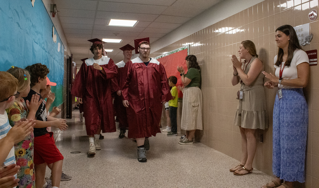 seniors in caps and gowns walk in hallway