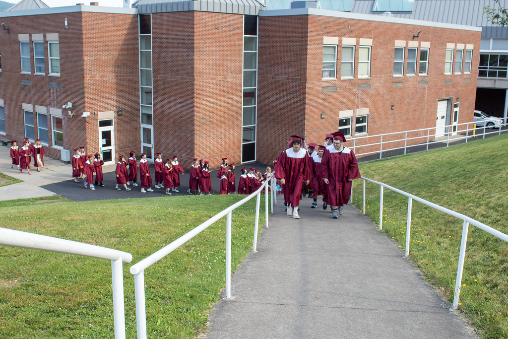 seniors in caps and gowns walk up  hill outside of school