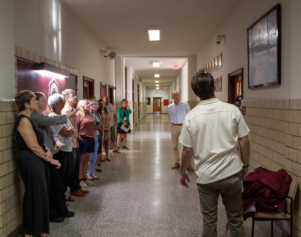 one of several adults watching gestures as she speaks about a painting that everyone is looking at