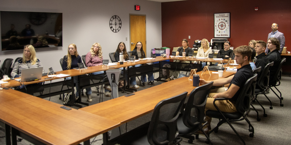 2 adults and 12 students around table, looking at screen