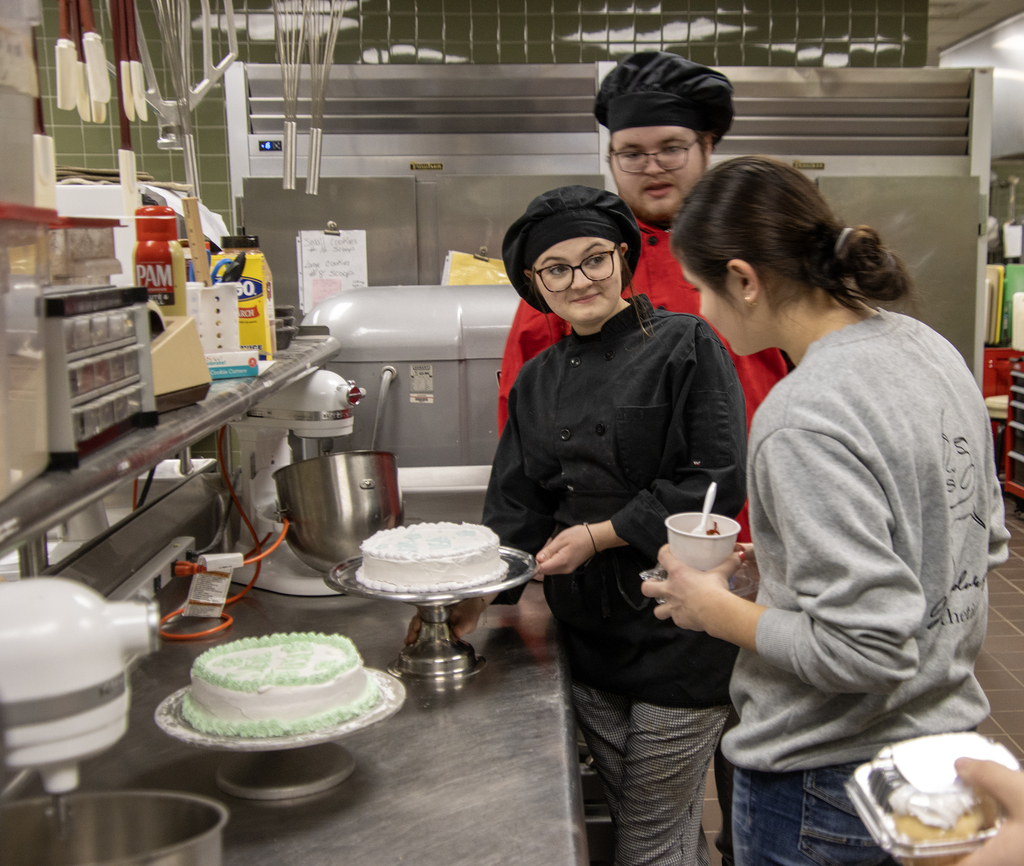 2 culinary students show cakes to visiting student